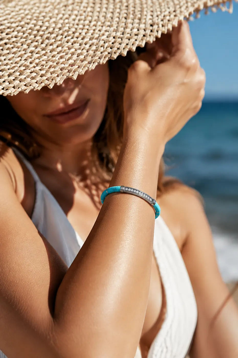 Bracelet Seal turquoise porté à la plage, chapeau de paille et mer en fond